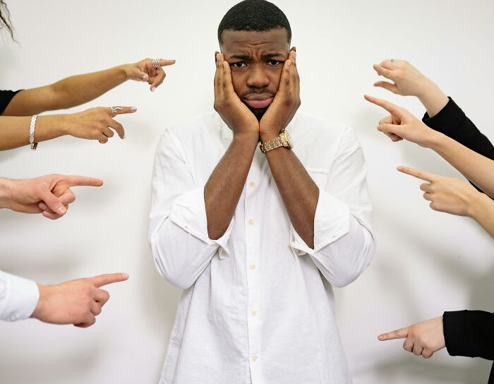 Man in white shirt looking stressed while surrounded by pointing fingers, symbolizing work skills people lack under pressure.