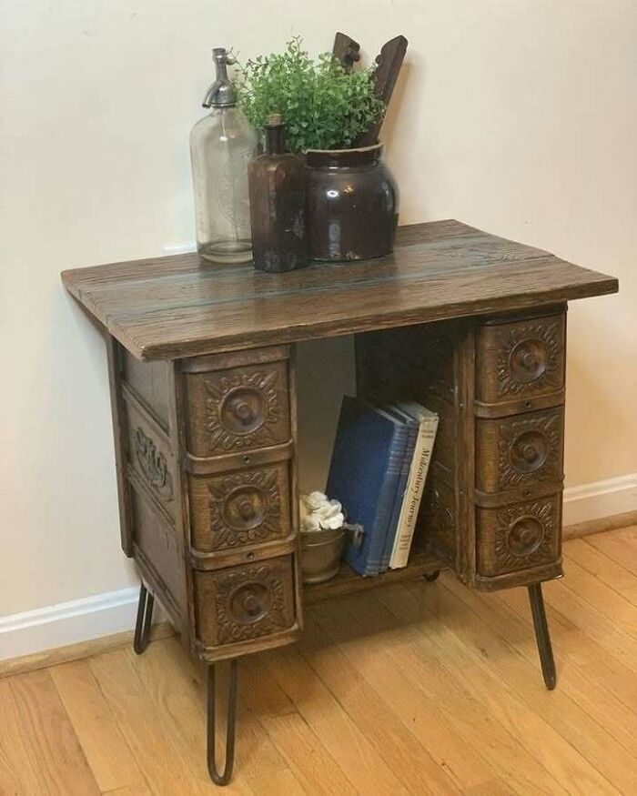 Recycled wooden cabinet with ornate drawers, topped with plants and glass bottles on a wooden floor.
