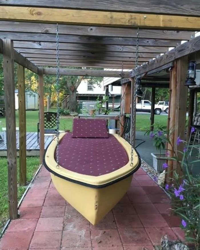 Repurposed boat transformed into a garden swing under a wooden canopy, highlighting creative recycling ideas.