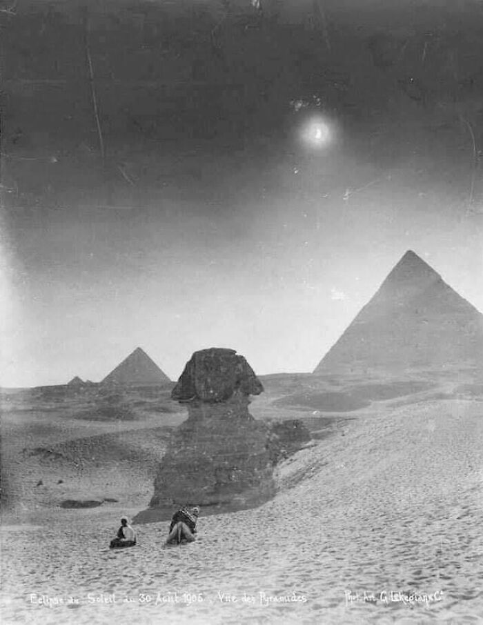 Historical photograph of the Sphinx and Pyramids under a solar eclipse, with two people in the foreground, taken in 1905.