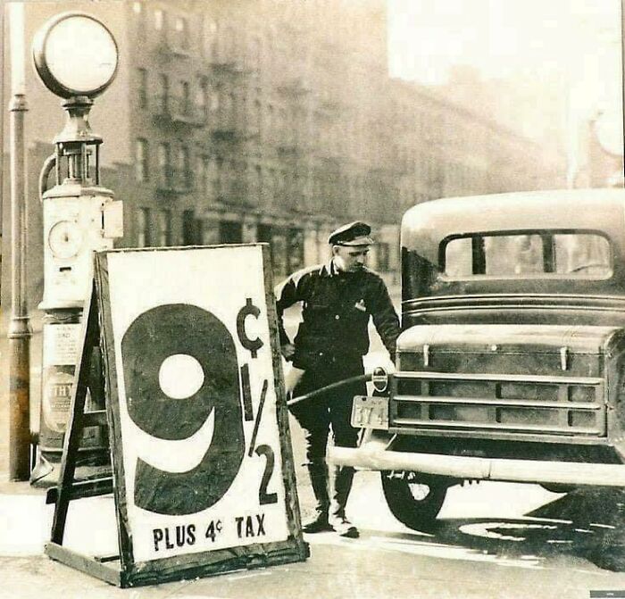 Historic gas station with signs showing 9½ cents per gallon plus tax, man refueling car nearby.