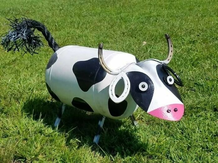 Recycled cow sculpture made from barrels, showcasing creative recycling on grass.