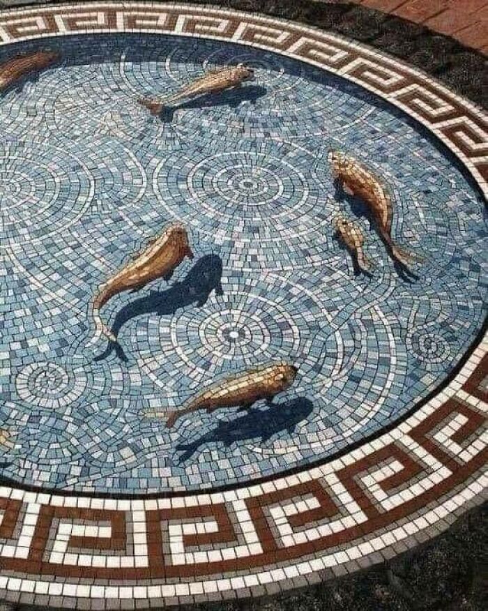 Historical mosaic showing fish in intricate circular design, with detailed geometric border pattern.