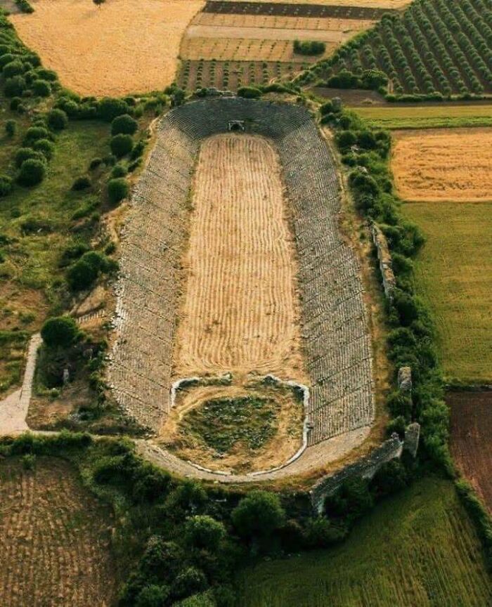 Ancient amphitheater ruins in a grassy field, showcasing historical events from the past.