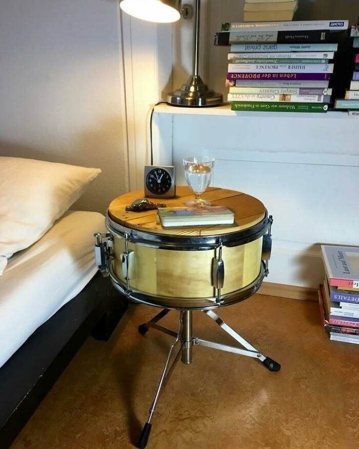 Drum repurposed as a bedside table with books and a lamp, inspiring recycling creativity.