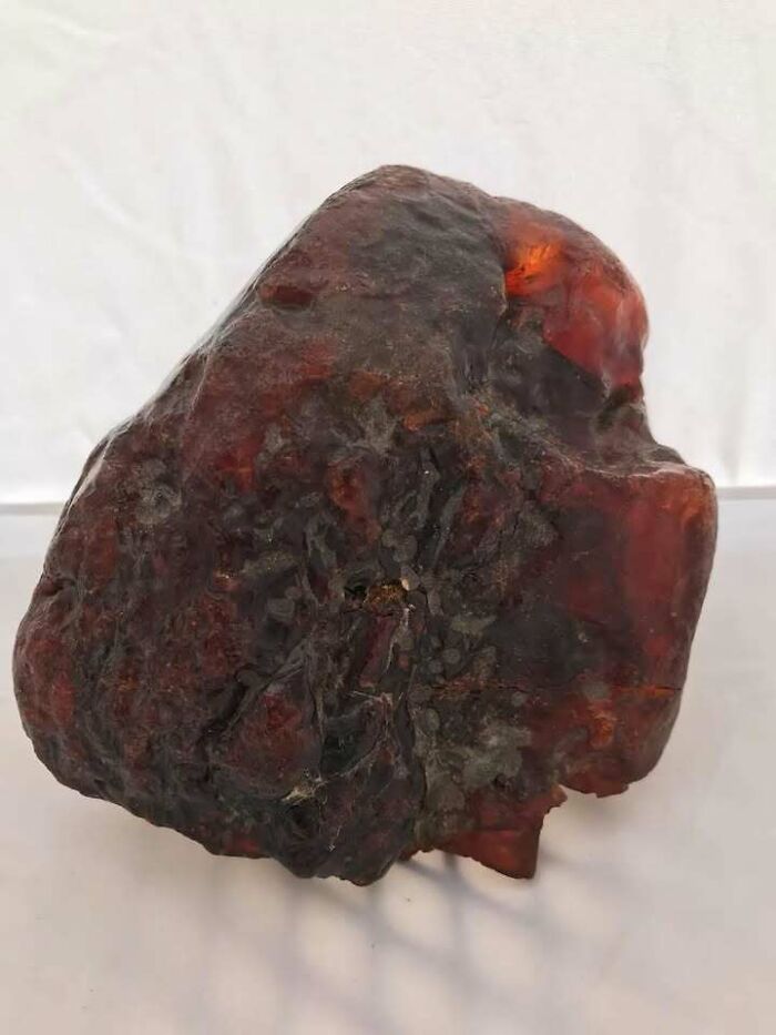 Large piece of historical amber with a rough texture and reddish hue, resting on a white surface.