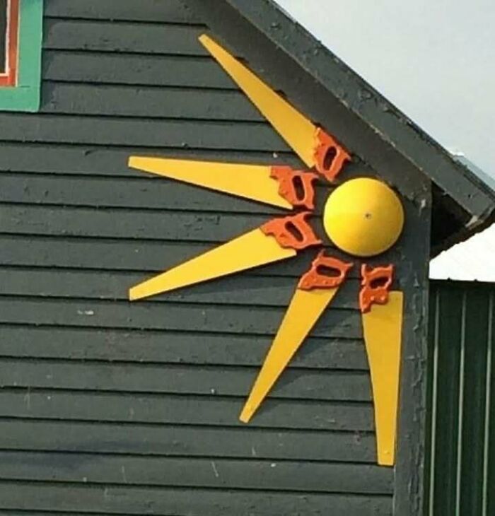 Creative recycling art on building wall, featuring a sun design with repurposed materials.