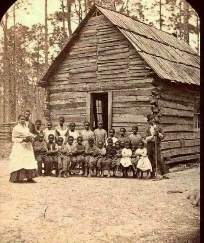 Historical photo of a group outside a wooden schoolhouse, showing an interesting moment in history.