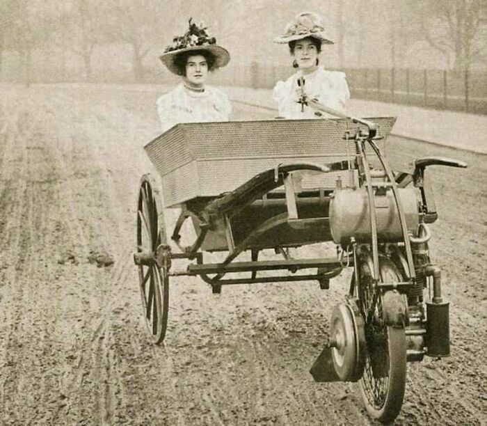Two women in vintage attire riding an early motor tricycle, showcasing interesting history.