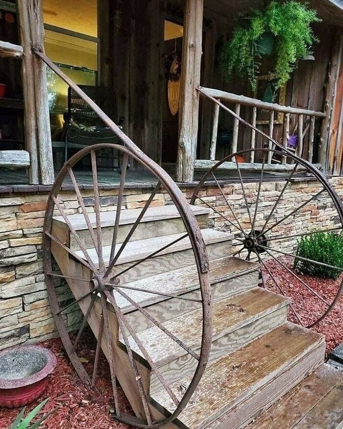 Rustic staircase with recycling-inspired wagon wheels as railing, surrounded by natural wood and greenery.