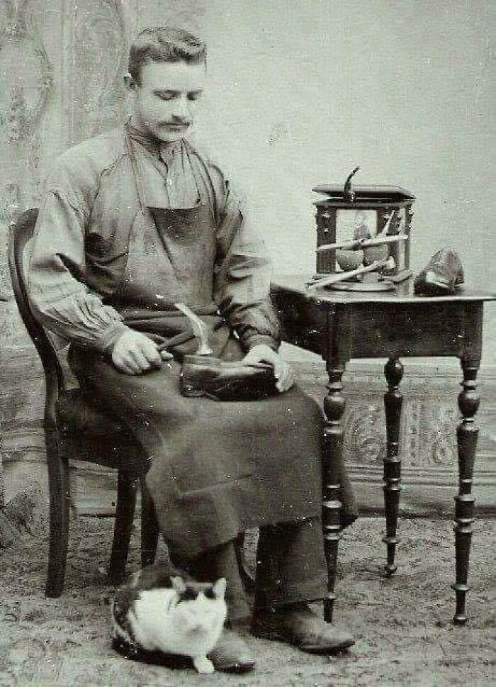 A shoemaker working at a bench, with tools and a cat, showcasing something interesting from history.
