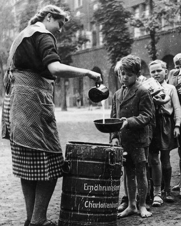 Woman pouring milk for children from a canister labeled Charlottenburg, capturing an interesting historical moment.