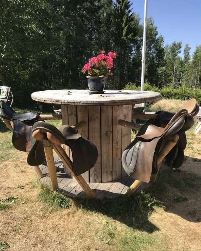 Recycled table made from wooden spool with saddle chairs, adorned with flowers, illustrating creative recycling ideas.