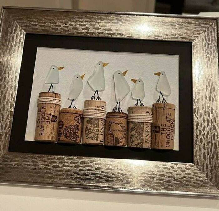 Framed artwork of birds made from recycled corks and glass, highlighting creative recycling.