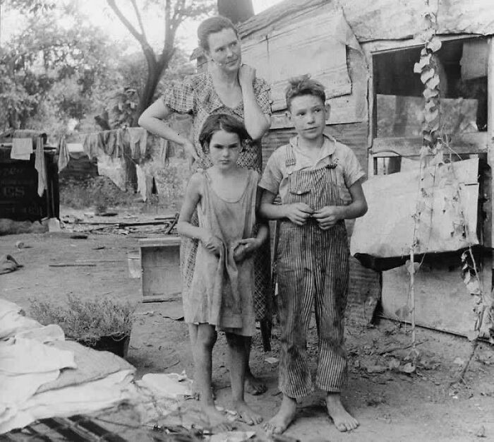 A historical moment showing a family in the Great Depression era standing outside their makeshift home.