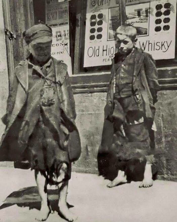 Barefoot children wearing tattered clothes stand outside a whisky shop, a scene illustrating interesting historical events.