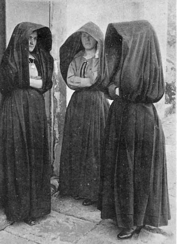 Three women in traditional hooded outfits, illustrating an interesting historical fashion moment.