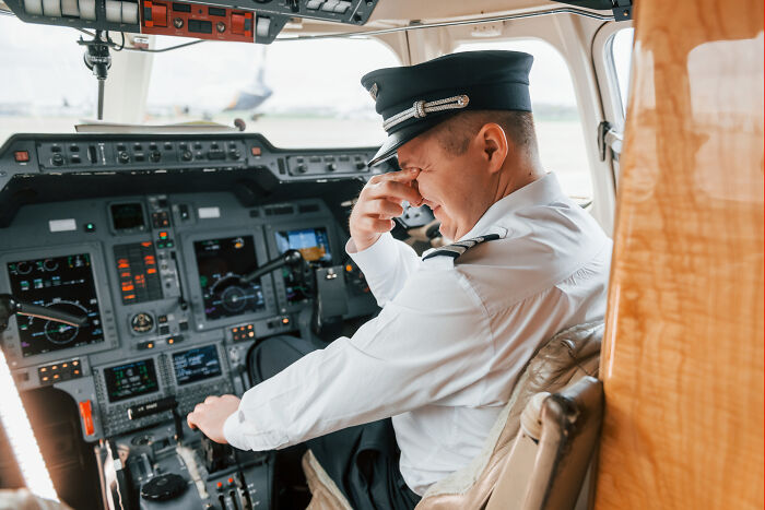 Pilot in cockpit, rubbing forehead, highlighting assumptions about people's jobs in aviation industry.