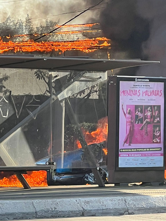 Bus shelter engulfed in flames after aviation disaster with plane crash nearby.