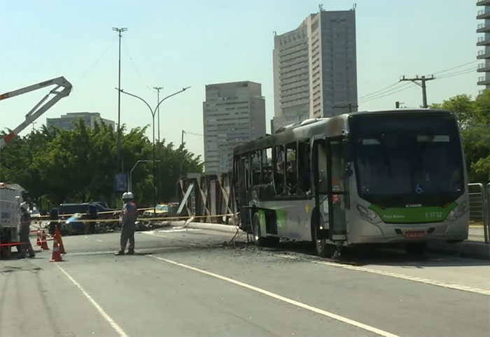 Bus damaged in aviation disaster, cordoned off on city street with surrounding skyscrapers.