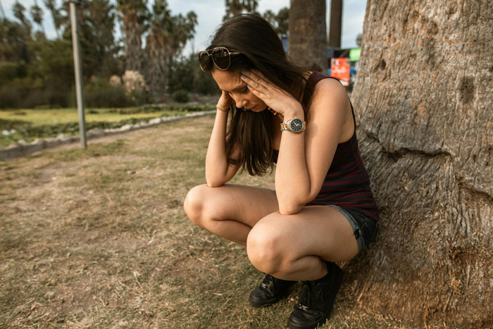A gay woman crouching by a tree, looking shocked and thoughtful outdoors. A gay woman crouching by a tree, looking shocked and thoughtful outdoors.