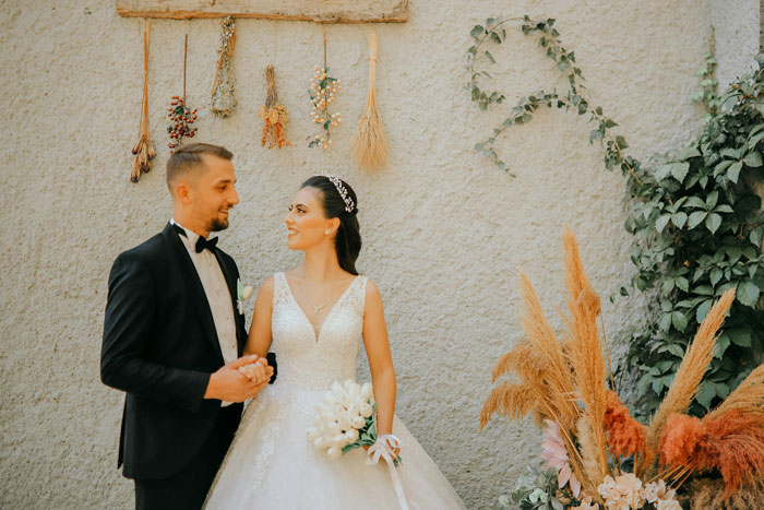 Bride and groom smiling in a garden setting with dried floral decorations, conveying wedding joy and celebration. Bride and groom smiling in a garden setting with dried floral decorations, conveying wedding joy and celebration.