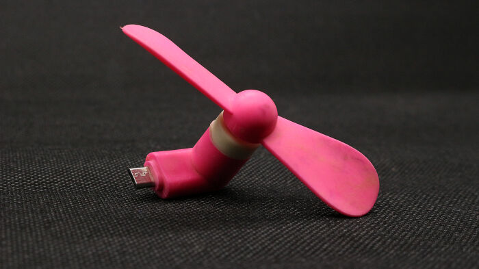 Portable pink USB mini fan on a dark textured surface, an essential for peaceful traveling.