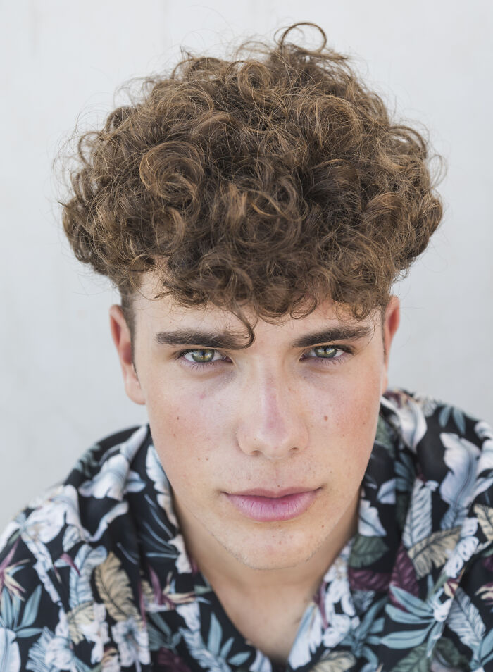 A person with curly hair in a floral shirt, representing recent fashion trends people hate.