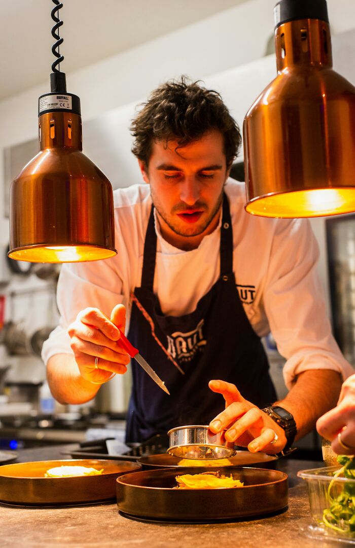 Chef plating dishes under warm lighting in a restaurant kitchen, focusing on culinary precision and technique.