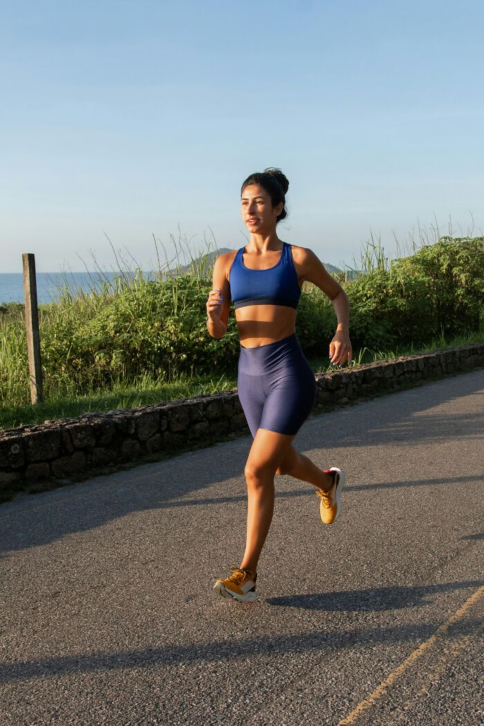 Person running outdoors on a sunny day, wearing blue athletic wear on a scenic path.