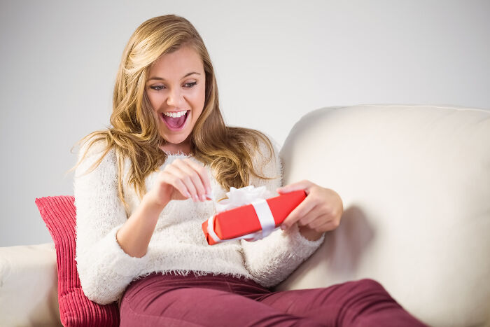 Woman delightedly opening a simple Valentine's gift on a couch.