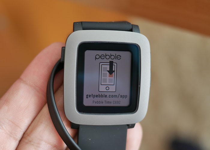 Pebble smartwatch, a good product that failed, held in hand displaying app download screen.