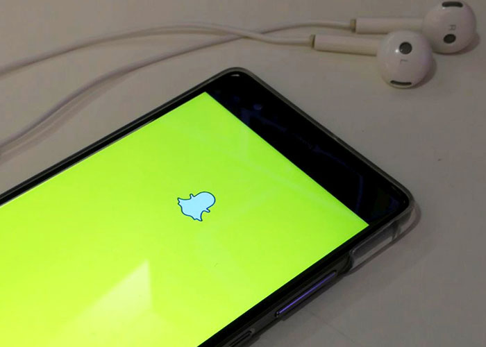 Smartphone displaying Snapchat, one of the products that failed despite being good, alongside white earbuds.