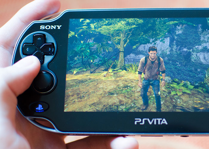 Hand holding a Sony PS Vita, a product that failed despite being good, displaying a video game scene.