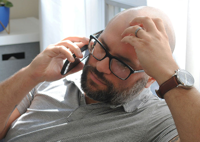 Man in glasses on a phone call, looking stressed, possibly discussing family BBQ and stepsiblings issue.