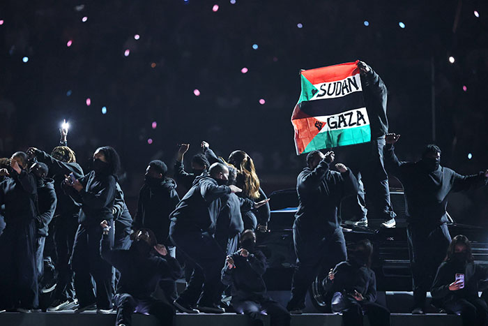 Performers at Super Bowl holding a Sudan and Gaza flag, contributing to an awkward and outrageous moment.