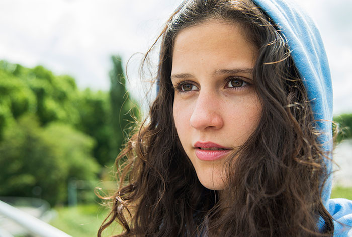 Teen in a blue hoodie outdoors, with a thoughtful expression, dealing with a challenging situation.