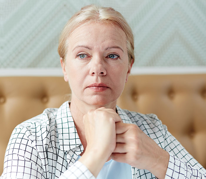 Woman looking thoughtful, sitting indoors, wearing a checkered shirt. Keywords: horrible mother.