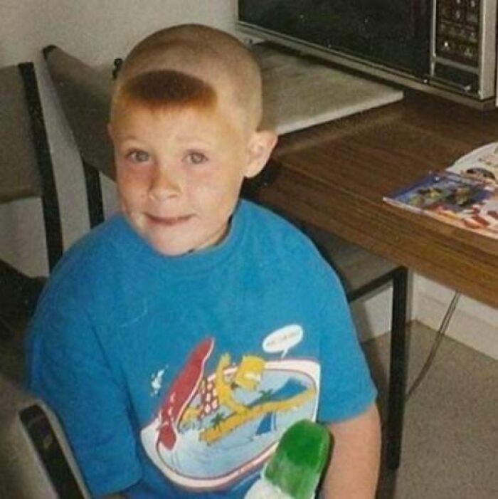 Child with a unique buzz cut in a blue shirt holding a green popsicle, showcasing an epic hair disaster from the 1980s.