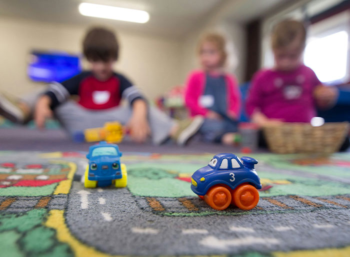 Children playing with toy cars on a colorful rug, focusing on a blue car in the foreground.