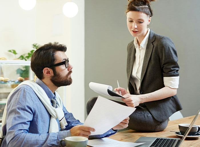 Two colleagues discussing documents at a desk, one wearing glasses, related to quitting job experiences.
