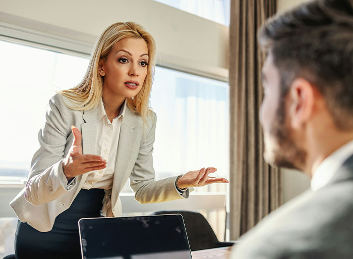 A woman in a gray blazer speaking assertively to a man, capturing a tense office moment related to quitting a job.