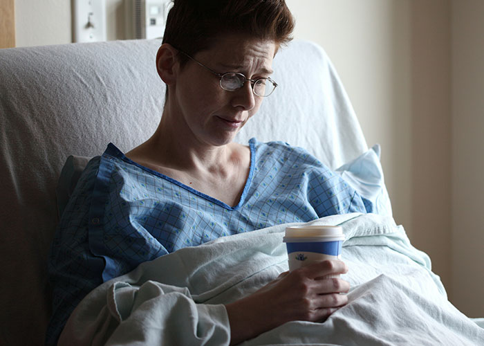 Person in hospital bed holding a coffee cup, appearing contemplative about quitting their job on the spot.