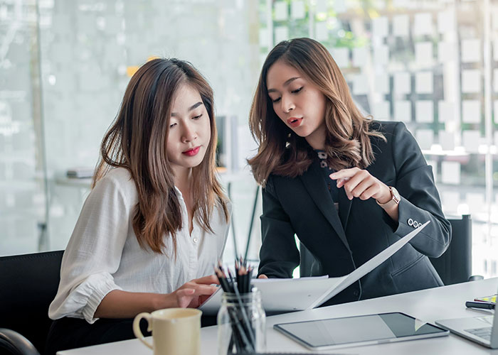 Two women in an office setting, reviewing documents, possibly discussing job resignation.