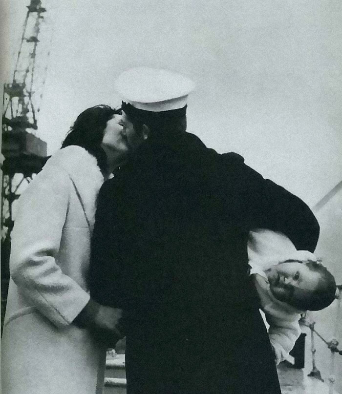 A sailor kisses a woman while holding a smiling baby, creating a moment from rare historical photos.