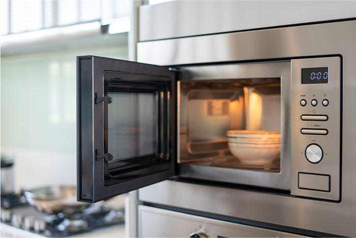Open microwave oven with a ceramic bowl inside in a modern kitchen illustrating doing something the wrong way.