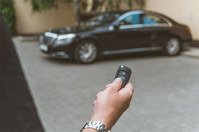 Hand holding a car key remote, pointing at a blurred luxury sedan in the background, possibly indicating a common mistake.