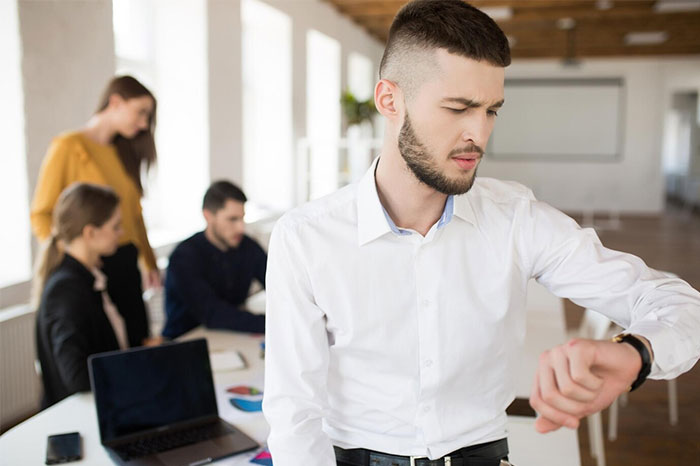 Man in white shirt checking watch during a meeting, representing doing something very wrong in time management.