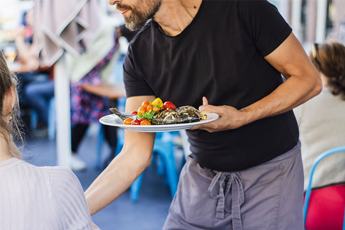 Man in black shirt serving food in a busy restaurant, illustrating moments people realized they were doing things wrong.