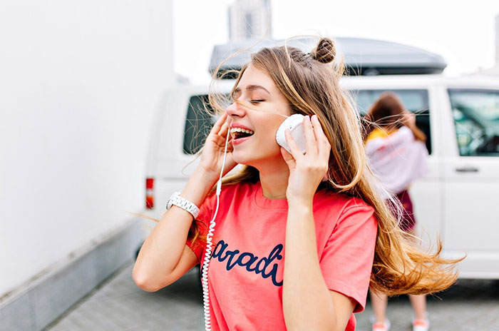 Woman holding half a coconut to her ear, smiling and standing near a white van.
